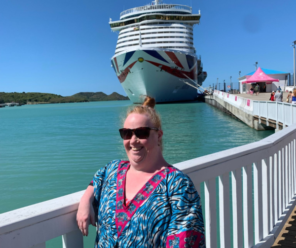 Victoria is standing in front of a huge cruise boat, which she's spending her holiday on! She is smiling brightly and wearing a colourful kaftan so they must be somewhere hot! This is what fostering adults looks like for Shared Lives carers.